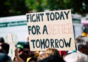 Crowd holding a protest sign with 'Fight Today for a Better Tomorrow', outdoors and during the day.